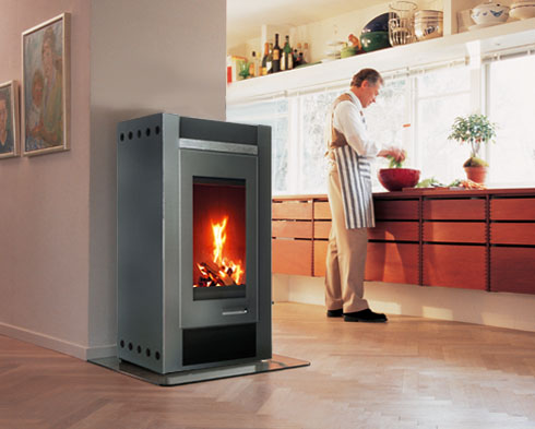 stufe a legna Nobus di skantherm, il cassetto per la cenere è nascosto dietro il grande sportello in vetro, rivestimento laterale in acciaio, stufa installata in grande ambiente cucina salotto in una casa tipica scandinava moderna
